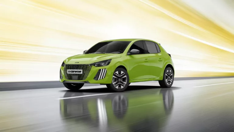 Grüner Peugeot Kleinwagen schräg von der Seite nach links fahrend auf grauer, spiegelnder Fläche mit gelbem Hintergrund.