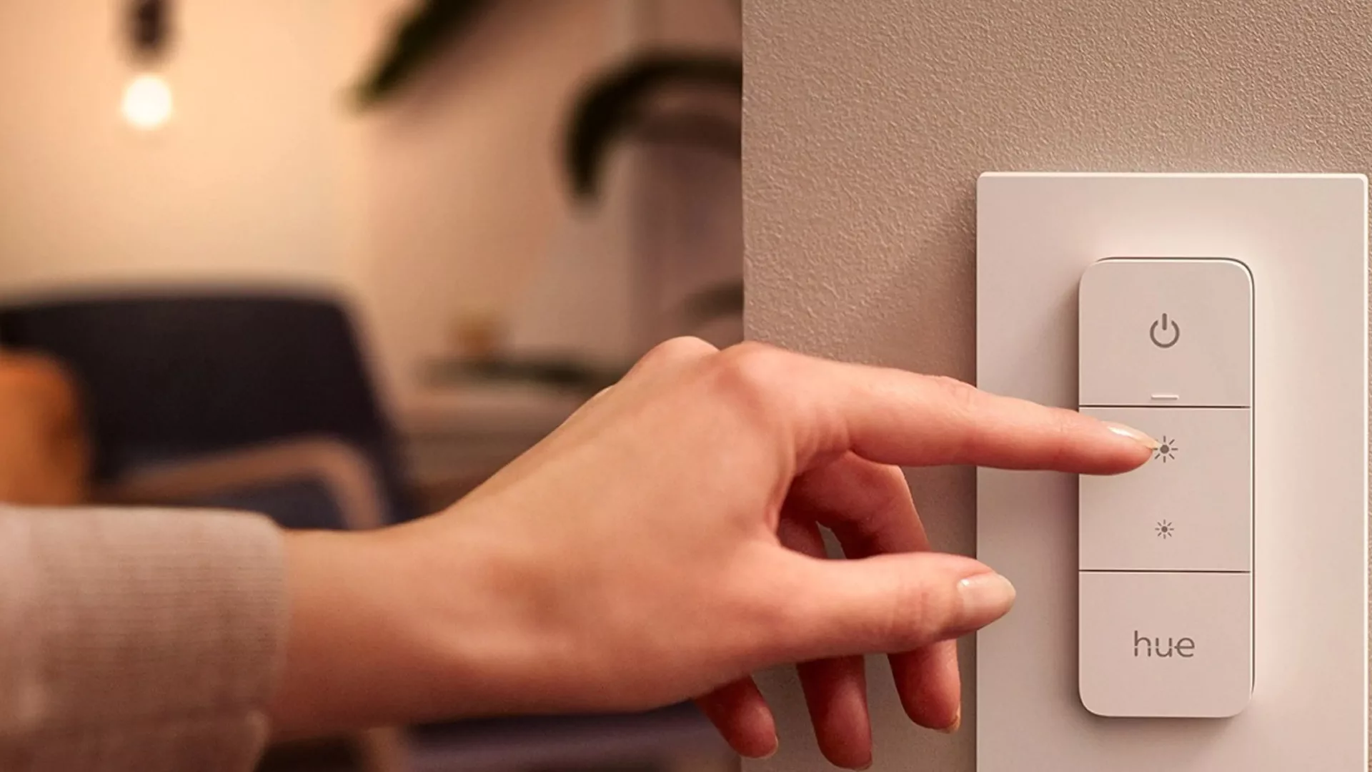 Eine Hand schaltet den Hue-Schalter, im Hintergrund leuchtet Licht. (@Philips)