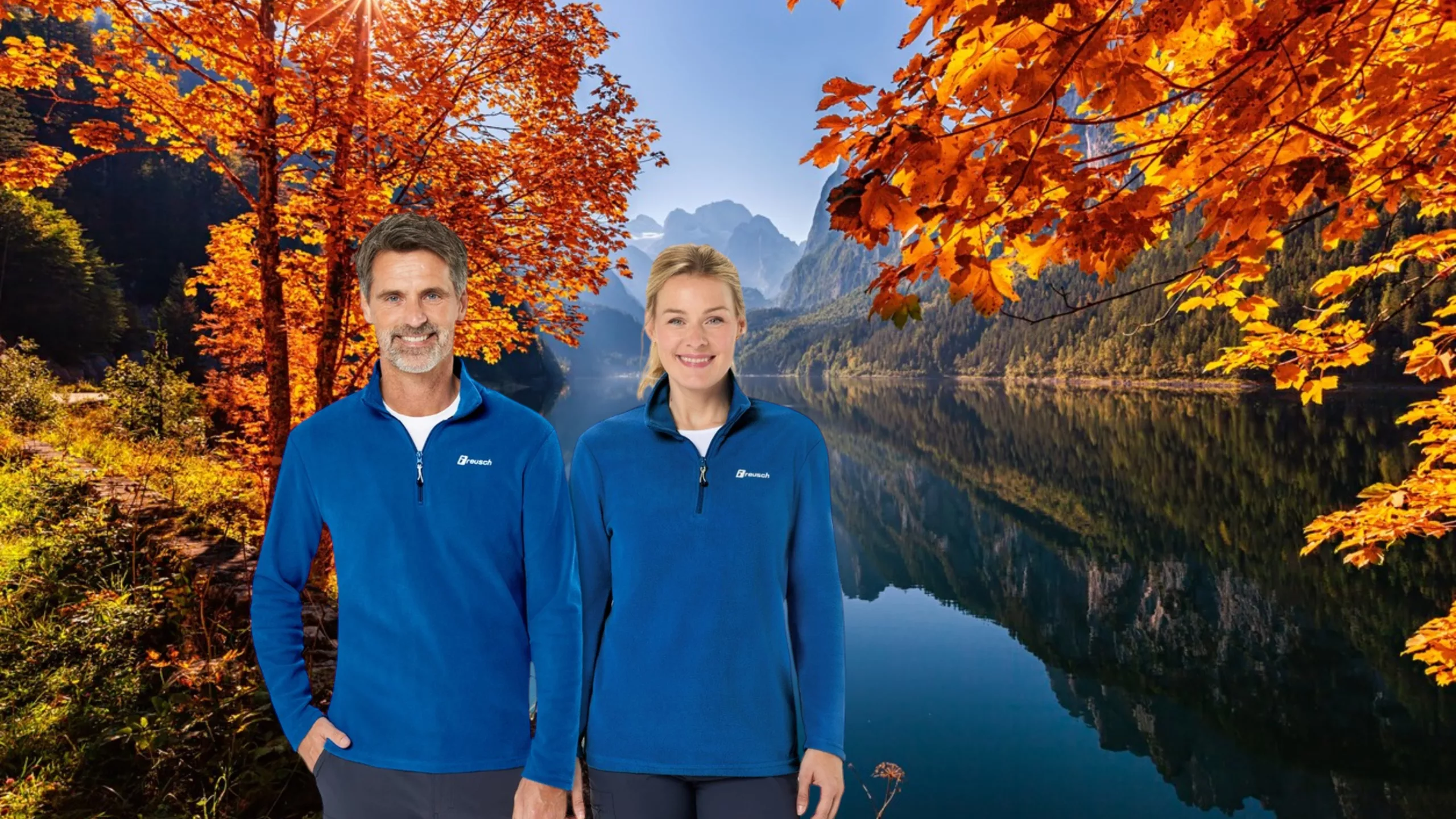 Ein Mann mit dunklen kurzen Haaren und grauem Bart mittleren Alters sowie eine Frau mit blondem Pferdeschwanz in blauen Fleeceshirts von vorne, nebeneinander stehend lächelnd. Vor herbstlicher Bergsee-Kulisse