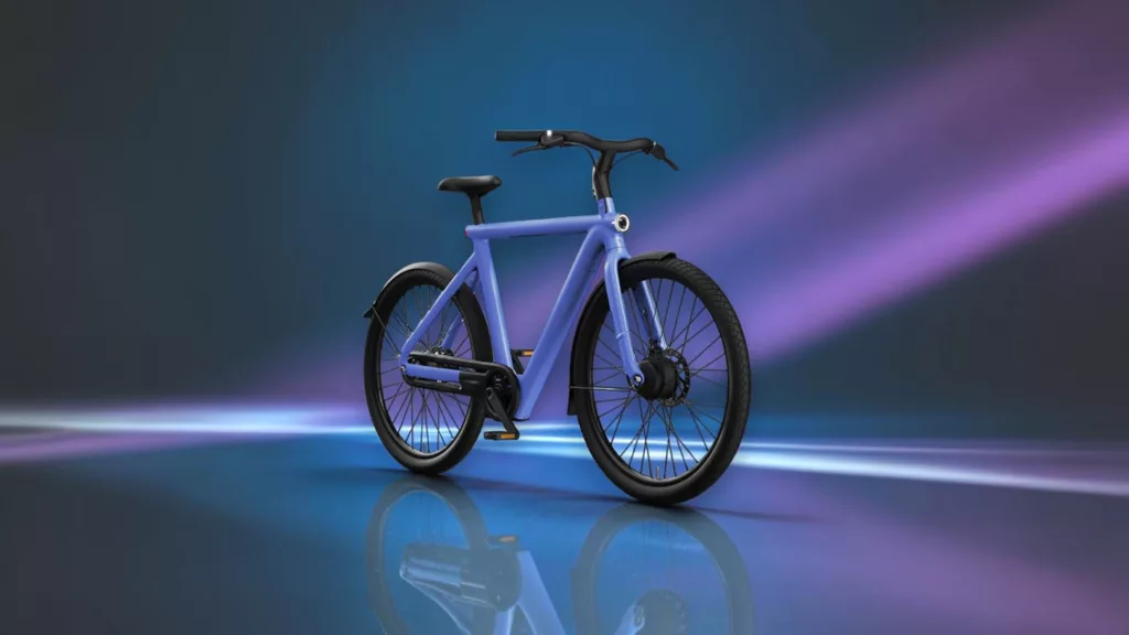 Hell-lila E-Bike von VanMoof schräg von der Seite nach rechts fahrend vor dunkelblauem Hintergrund mit lila Lichtstreifen auf dunkler spiegelnder Fläche