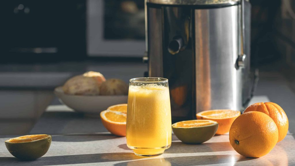 Frisch gepresster Orangensaft im Glas und Entsafter